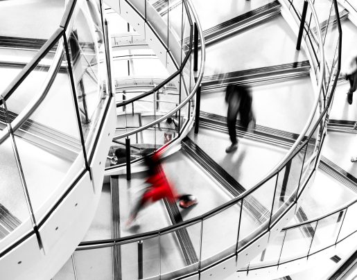 High angle image depicting an abstract view of a group of people running down a modern spiral staircase in the city. The running is depicted as motion blur, which makes it looks as though the people are moving extremely fast. Everything in the image is desaturated except one female who is dressed entirely in red. Room for copy space. ***IMAGE SHOT IN CITY HALL, LONDON, UK, A PUBLICLY OWNED BUILDING FREELY ACCESSIBLE TO THE PUBLIC. PLEASE NOTE THERE NO FEES OR TICKETS ARE REQUIRED TO ENTER, AND THERE ARE NO PHOTOGRAPHIC RESTRICTIONS***